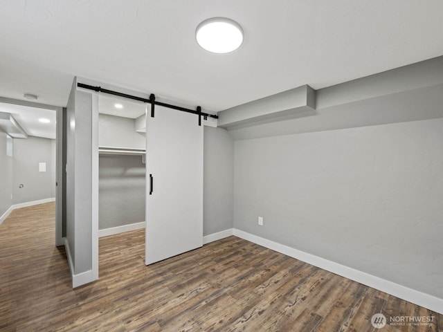 unfurnished bedroom featuring wood finished floors, a barn door, baseboards, a closet, and a walk in closet