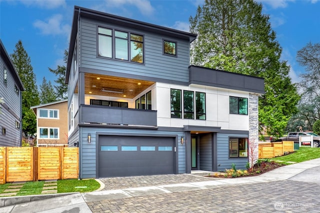 contemporary house with a balcony, fence, an attached garage, and driveway
