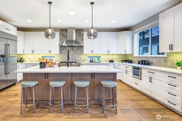 kitchen with wall chimney exhaust hood, appliances with stainless steel finishes, a kitchen island, a kitchen breakfast bar, and white cabinets