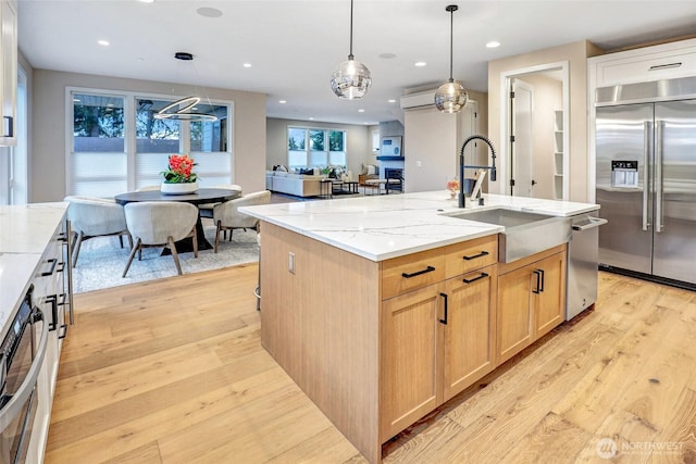 kitchen with appliances with stainless steel finishes, a sink, light wood-style flooring, light stone counters, and recessed lighting