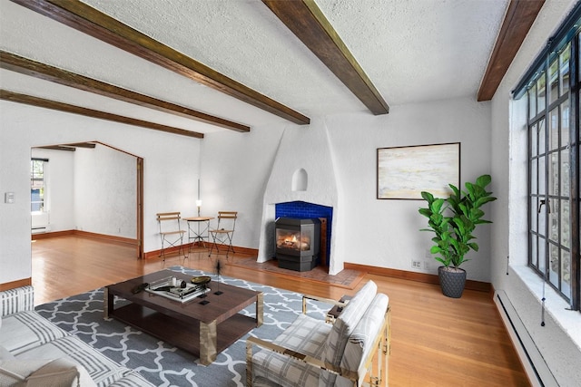 living room with baseboard heating, wood finished floors, a textured ceiling, beam ceiling, and a fireplace