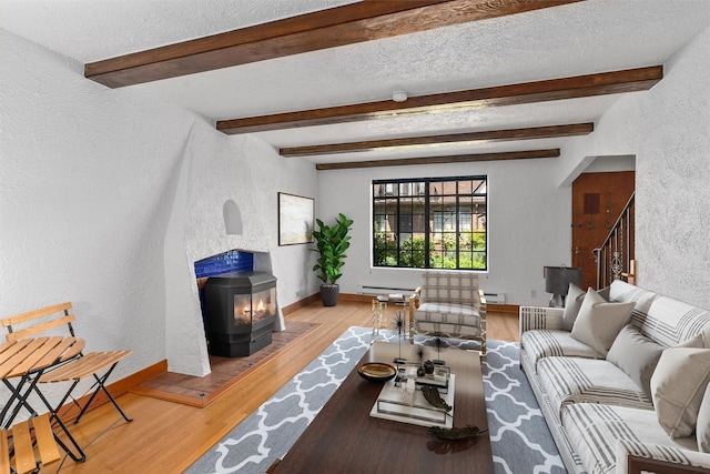 living area with a textured wall, baseboard heating, a baseboard radiator, a wood stove, and wood finished floors