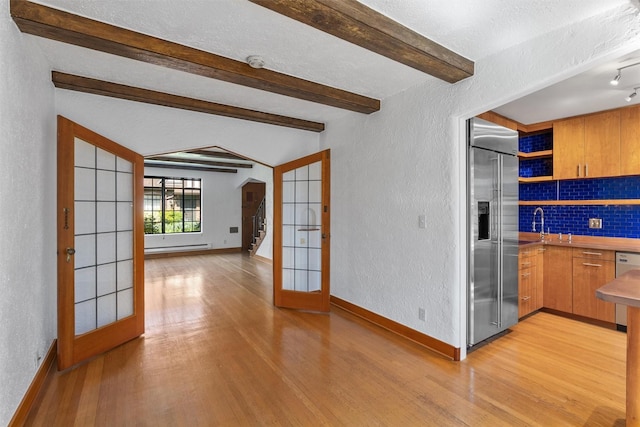 kitchen with built in refrigerator, a textured wall, french doors, light wood finished floors, and baseboards