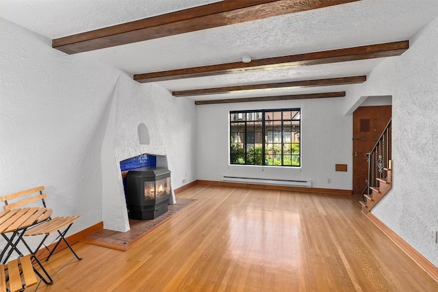 unfurnished living room with a baseboard heating unit, a wood stove, a textured wall, wood finished floors, and stairway