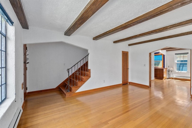 unfurnished living room featuring a baseboard heating unit, a textured ceiling, arched walkways, wood finished floors, and baseboards