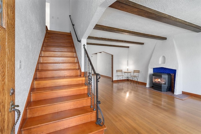 stairway with a textured wall, wood finished floors, beam ceiling, a large fireplace, and a textured ceiling