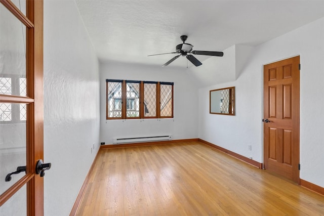 spare room featuring baseboard heating, light wood finished floors, a ceiling fan, and baseboards