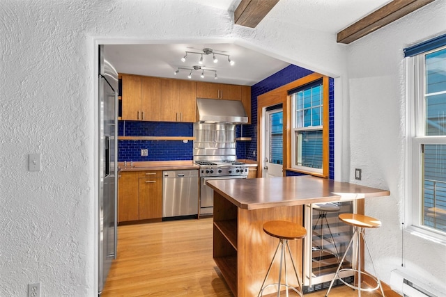 kitchen with a textured wall, appliances with stainless steel finishes, under cabinet range hood, open shelves, and tasteful backsplash