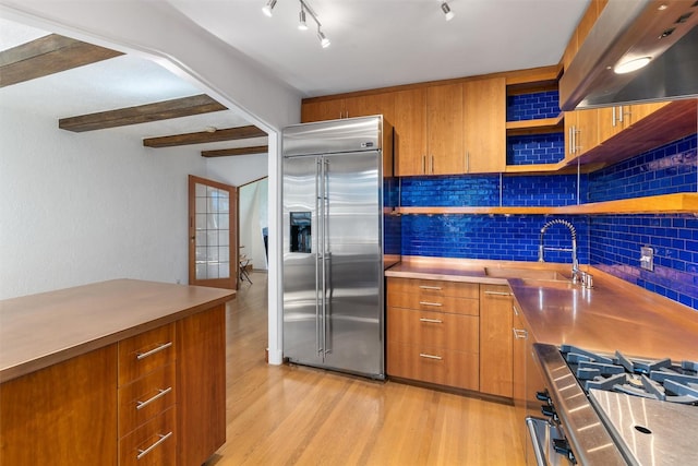 kitchen featuring appliances with stainless steel finishes, ventilation hood, open shelves, light wood-style floors, and backsplash