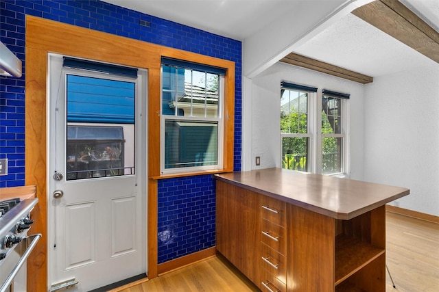 kitchen featuring light wood-style floors, stainless steel counters, open shelves, brown cabinets, and a peninsula