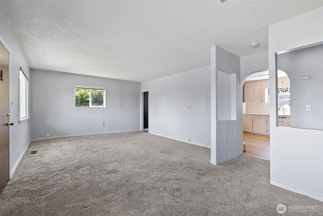 3510 N Puget Sound Ave, Tacoma, WA 98407 - carpeted empty room featuring a textured ceiling, baseboards, a sink, and arched walkways