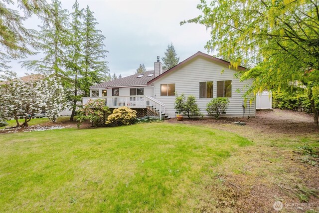 back of property featuring a chimney, a wooden deck, and a yard