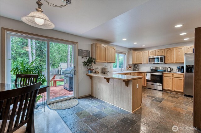 20282 NW Cedar Ln, Poulsbo, WA 98370 - kitchen with stainless steel appliances, a peninsula, light brown cabinetry, stone tile flooring, and light countertops