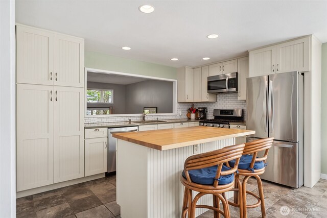 kitchen featuring stainless steel appliances, wooden counters, a sink, a kitchen breakfast bar, and a kitchen island
