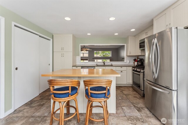 kitchen with appliances with stainless steel finishes, a sink, decorative backsplash, white cabinets, and ceiling fan