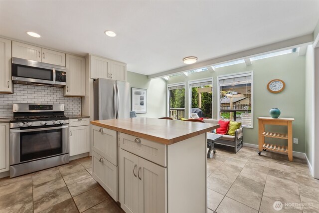 kitchen with appliances with stainless steel finishes, backsplash, a kitchen island, baseboards, and recessed lighting
