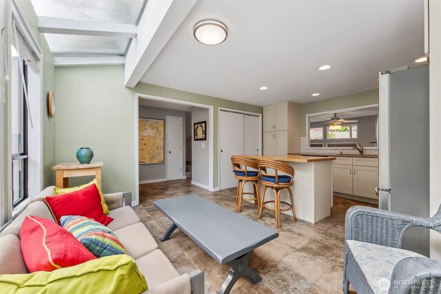 living area featuring stone finish flooring, beam ceiling, baseboards, a ceiling fan, and recessed lighting