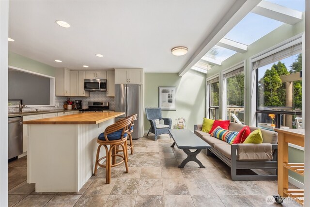 kitchen with wooden counters, stainless steel appliances, decorative backsplash, a center island, and a breakfast bar