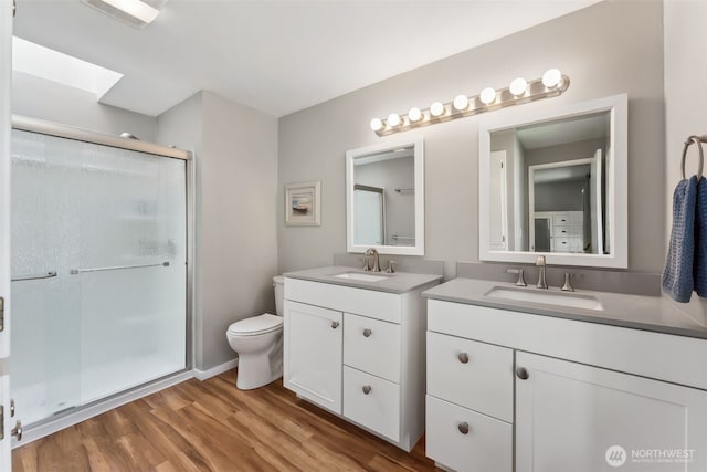 bathroom with a stall shower, two vanities, wood finished floors, toilet, and a skylight