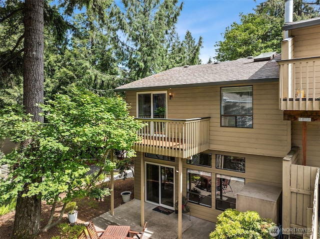 rear view of property featuring a balcony, a patio, and roof with shingles