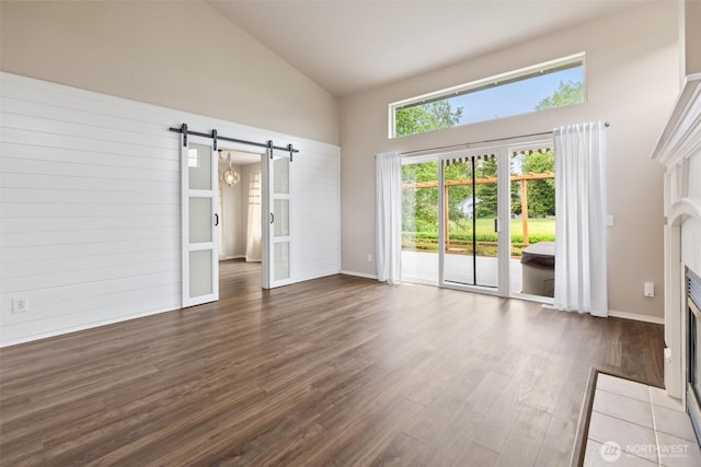 7521 Sterling Pl, Arlington, WA 98223 - spare room featuring high vaulted ceiling, a barn door, dark wood-type flooring, a fireplace with flush hearth, and baseboards