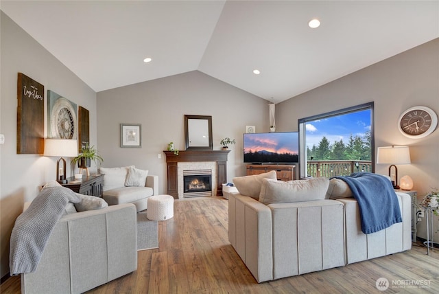living area featuring lofted ceiling, a stone fireplace, wood finished floors, and recessed lighting