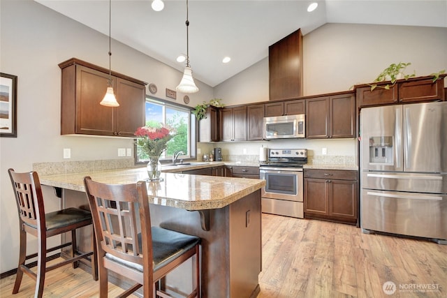 kitchen featuring appliances with stainless steel finishes, a peninsula, a sink, light wood-type flooring, and a kitchen breakfast bar