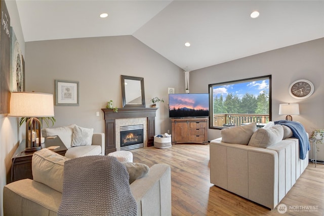 living room with vaulted ceiling, a tile fireplace, light wood-type flooring, and recessed lighting