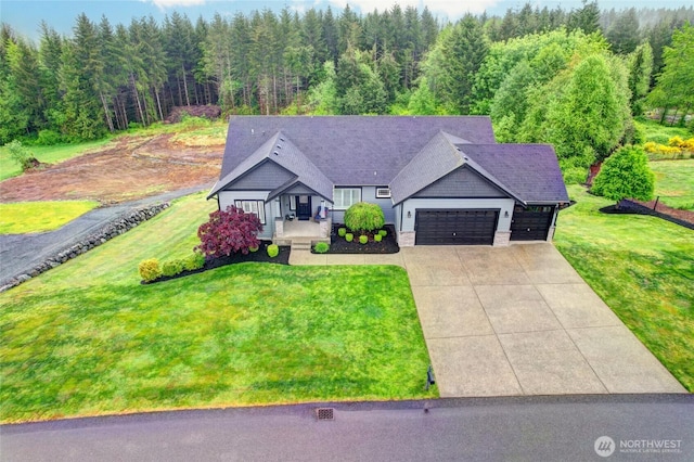 view of front of home featuring a garage, a front lawn, concrete driveway, and a wooded view