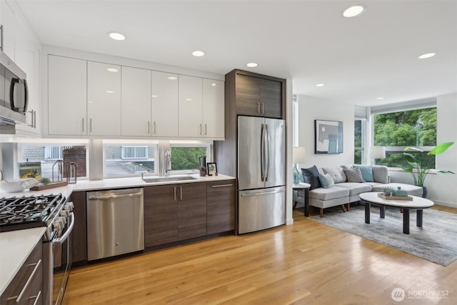 kitchen featuring stainless steel appliances, a sink, modern cabinets, light wood-style floors, and light countertops