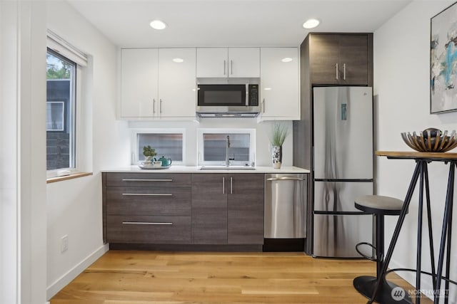 kitchen featuring stainless steel appliances, a sink, white cabinets, dark brown cabinetry, and recessed lighting