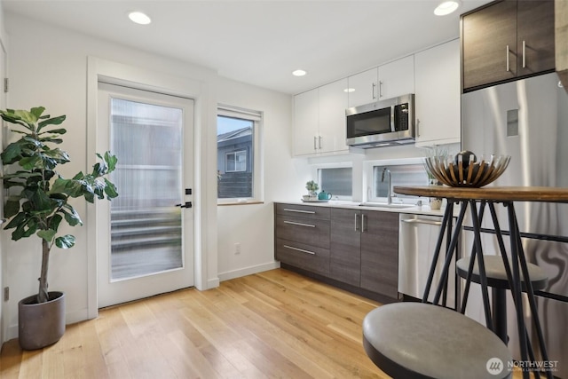 kitchen featuring appliances with stainless steel finishes, a sink, light wood-type flooring, white cabinets, and dark brown cabinets