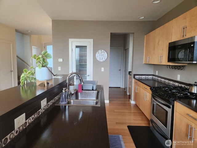 kitchen featuring stainless steel appliances, a sink, light wood-style flooring, dark countertops, and recessed lighting