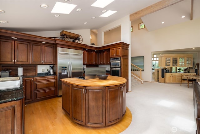 kitchen with stainless steel appliances, wooden counters, high vaulted ceiling, a kitchen island, and a sink