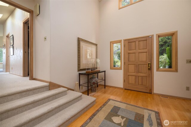 foyer entrance featuring wood finished floors, stairway, baseboards, and a high ceiling