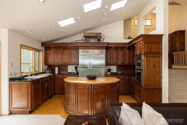 kitchen featuring stainless steel appliances, a sink, a skylight, vaulted ceiling, and a center island