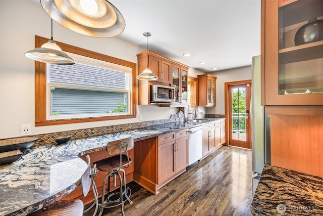 kitchen with stainless steel microwave, dishwasher, a sink, dark stone counters, and glass insert cabinets