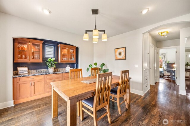 dining area with dark wood-style floors, arched walkways, and baseboards
