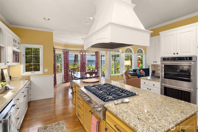 kitchen with stainless steel appliances, light wood-style floors, wainscoting, healthy amount of natural light, and light stone counters