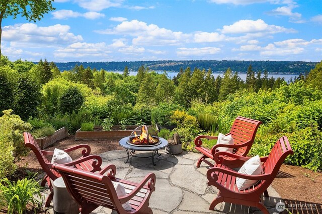 view of patio with an outdoor fire pit, a view of trees, and a water view
