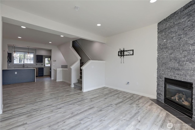 23120 SE Black Nugget Rd Unit A2, Issaquah, WA 98029 - unfurnished living room featuring light wood-type flooring, recessed lighting, stairs, a stone fireplace, and a sink