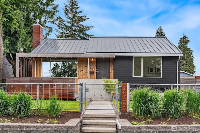 view of front of house featuring a gate, a fenced front yard, a chimney, a standing seam roof, and metal roof