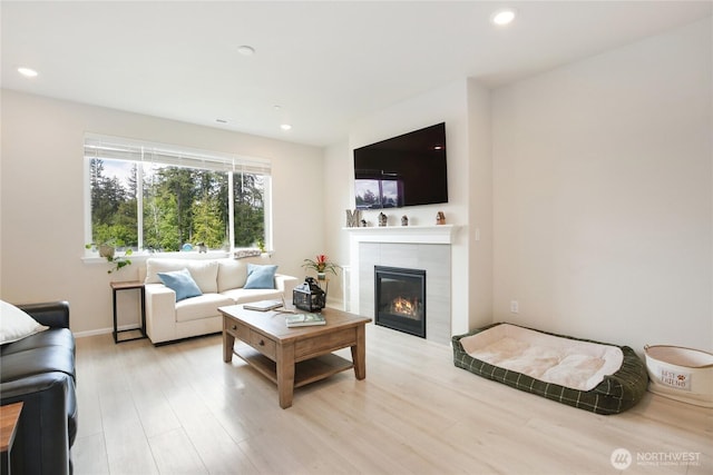 living area featuring a tiled fireplace, light wood finished floors, recessed lighting, and baseboards