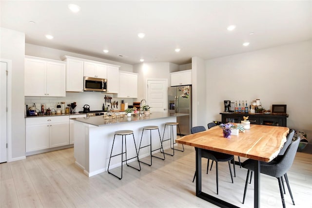 kitchen featuring appliances with stainless steel finishes, an island with sink, white cabinets, light wood-style flooring, and recessed lighting