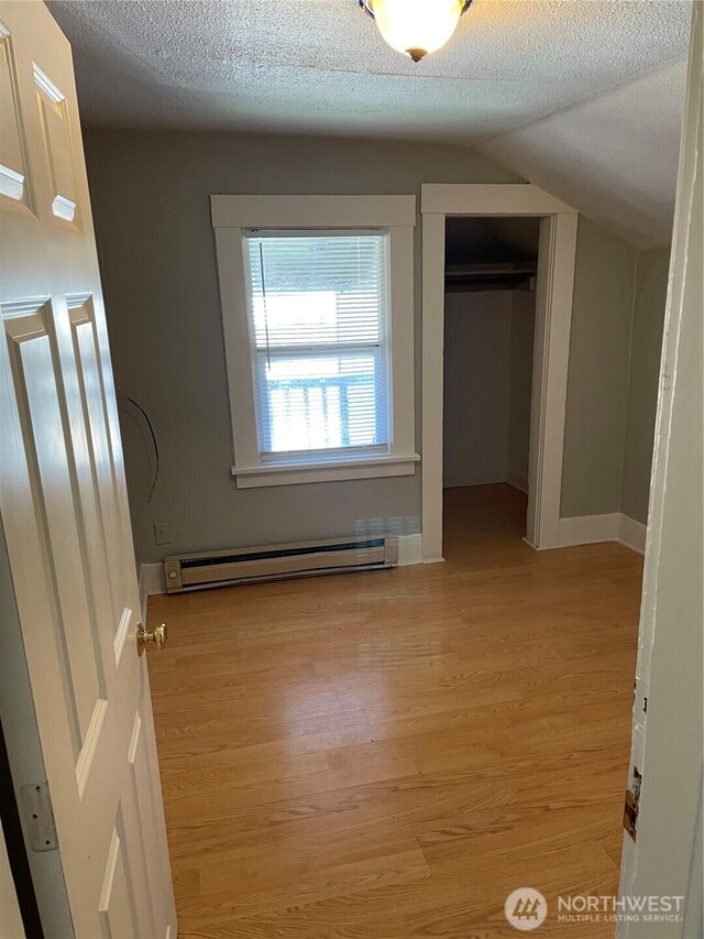 328 S Division St, Auburn, WA 98001 - unfurnished bedroom with baseboard heating, wood finished floors, a closet, vaulted ceiling, and a textured ceiling