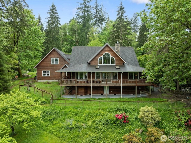rear view of property with a chimney, a yard, and roof with shingles