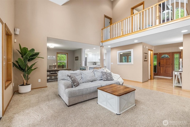 living area featuring light carpet, a high ceiling, and baseboards