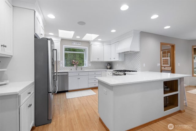 kitchen featuring stainless steel appliances, custom exhaust hood, light wood finished floors, decorative backsplash, and white cabinets