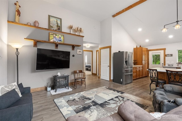 living area featuring a wood stove, beam ceiling, wood finished floors, high vaulted ceiling, and baseboards