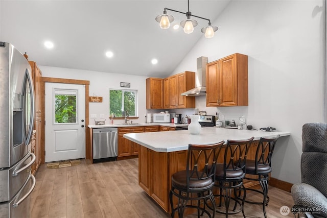 kitchen with stainless steel appliances, wall chimney range hood, a peninsula, a sink, and light countertops